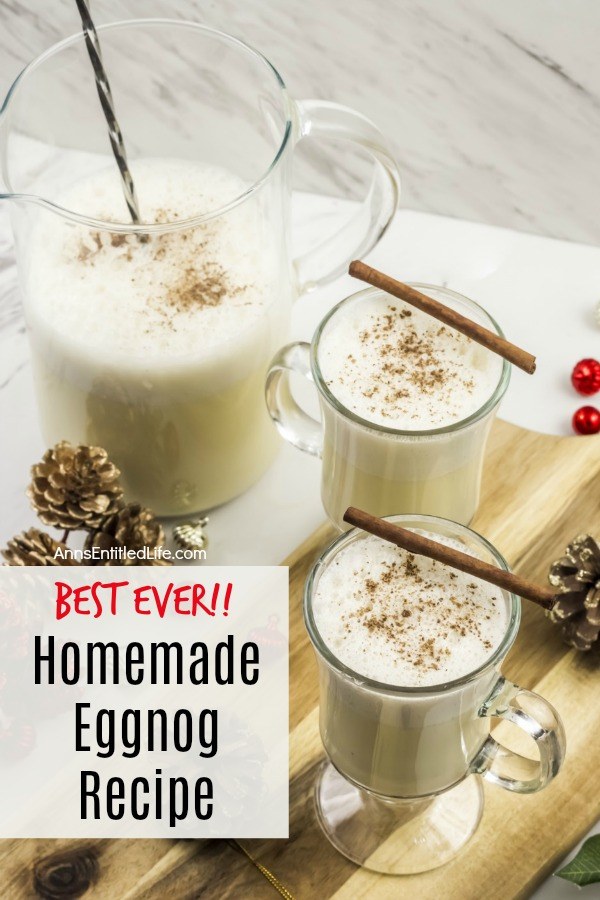pitcher of homemade eggnog and two poured glasses on a butcher block, with pinecone and red bulbs scattered about