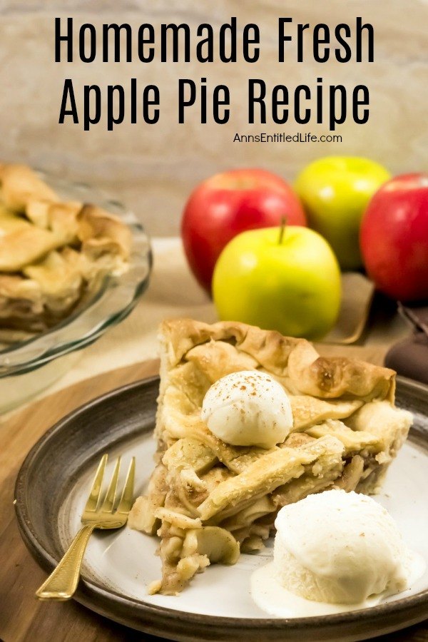 A homemade apple pie with a lattice top with one piece removed sits in the upper left. The plated pie of apple pie is served with a scoop of vanilla ice cream and sits on a dark plate. There are 3 fresh apples behind the pie. All this sits on a wooden board.
