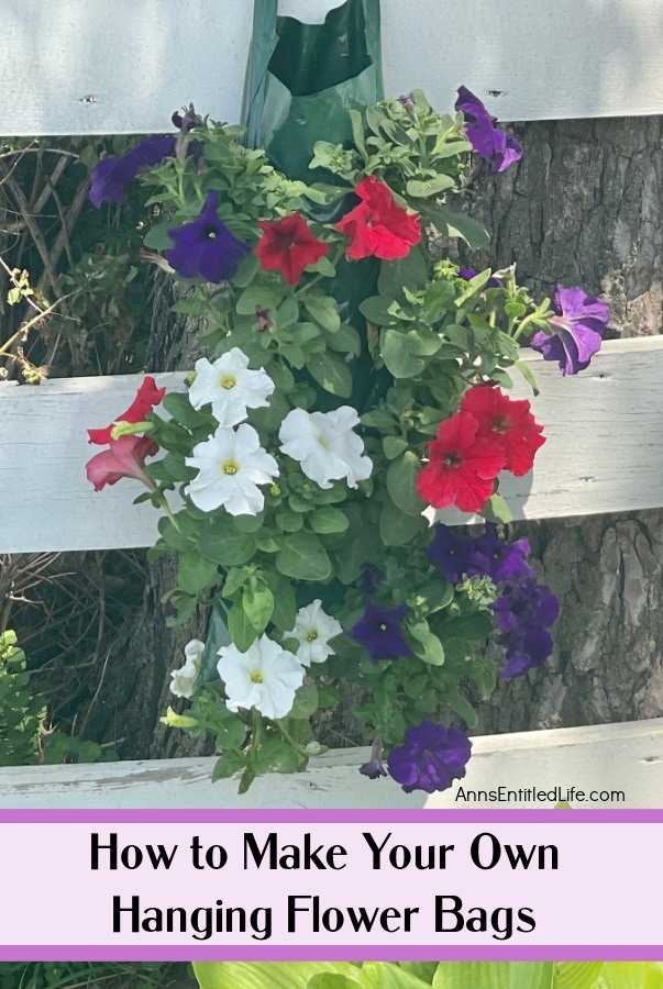a hanging flower pouch filled with red, white, and purple petunias hanging on a white fence with a tree trunk in the background