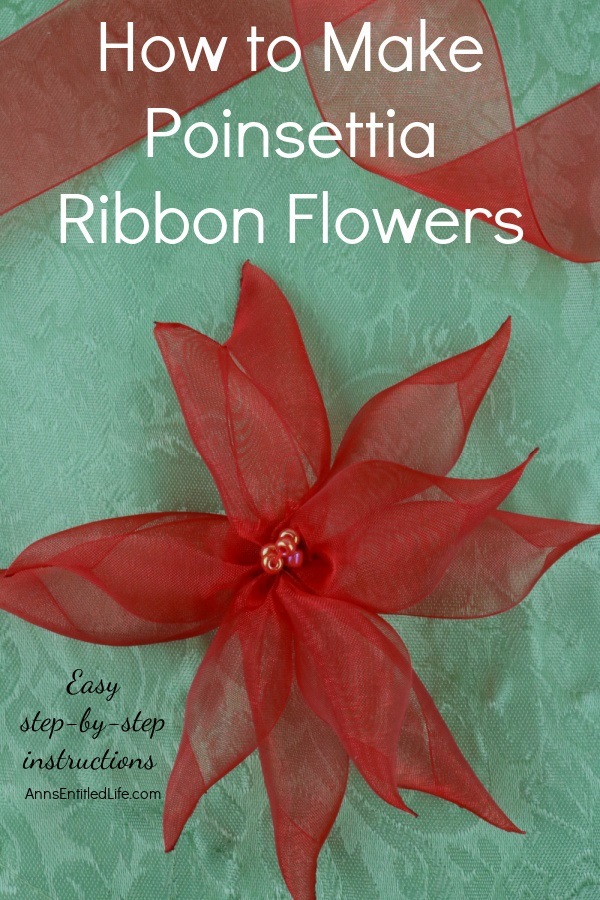 One red poinsettia ribbon flower sits on a green background. There is a length of red ribbon at the top.