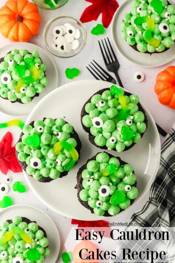 Overhead view of six cauldron cakes on a white plates, surrounded by forks and candy eyes.