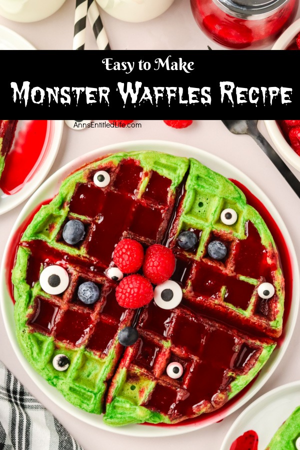 An overhead view of a stack of green waffles drenched in red syrup on a white plate. The waffles are topped with berries and candy eyes.