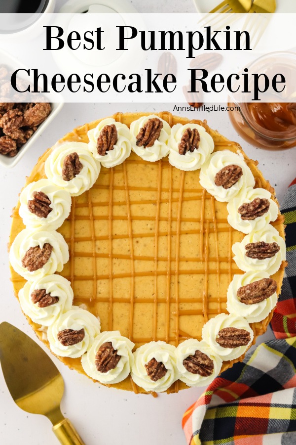 Overhead view of a whole pumpkin cheesecake, a pie lift in the lower left, a napkin in the lower right, some pecans in the upper left, and a jar of caramel sauce is in the upper right.