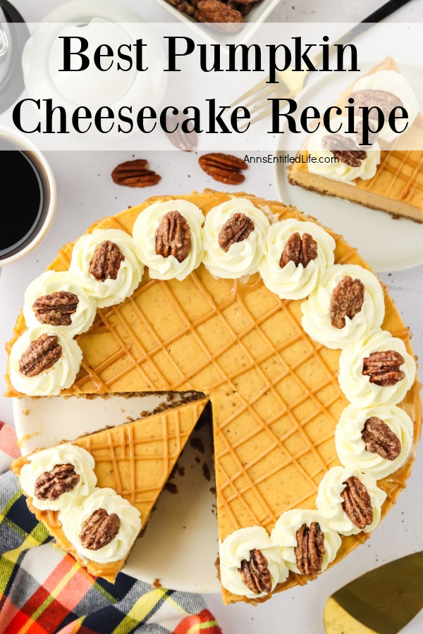 Overhead view of a pumpkin cheesecake, one piece is removed, another piece is cut on the white serving tray. a pie lift in the lower right, a napkin in the lower left, some pecans in the upper left, and a jar of caramel sauce is in the upper right.