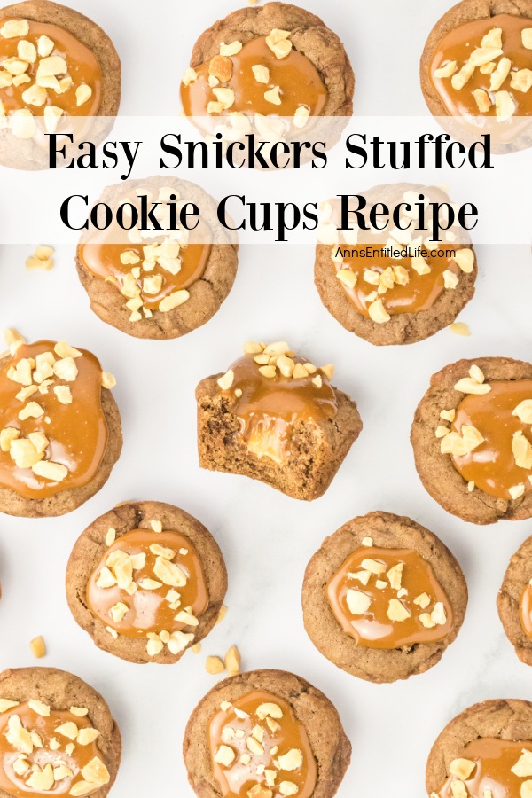 A dozen snickers stuffed cookie cups on a white board, the middle one has an open piece to see the inside