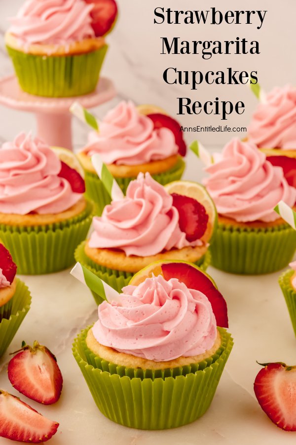 seven decorated strawberry margarita cupcakes on a flat white surface with strawberry slices inter-disbursed around the cupcakes.