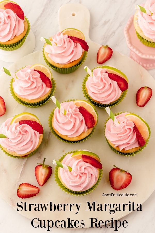 an overhead view of decorated strawberry margarita cupcakes on a white surface, several cut slices of fresh strawberries are inner-disbursed around them.