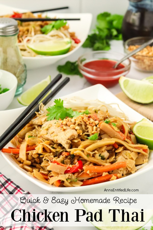 Side view of a servings of chicken pad Thai on a white plate, chopsticks are resting on the corner of the plate. There is a second serving in the upper left, red sauce, lime wedge, and peanuts in a bowl in the upper right.