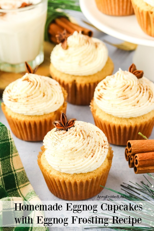 4 eggnog cupcakes on a white plate, more are on a cake stand in the upper right, there is a glass of eggnog in the upper left.